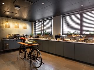 Espace buffet petit-déjeuner moderne à l'Elite Hotel Arcadia Stockholm avec armoires grises, suspensions et table vélo décorative.