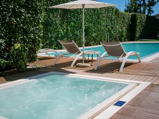 Zone piscine de l'hôtel Palazzo del Garda avec jacuzzi bouillonnant au premier plan, deux chaises longues sous parasol sur terrasse en bois.