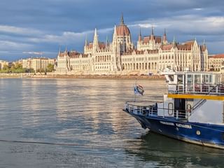 Bateau de croisière MS Princess Katharina sur le Danube avec le Parlement hongrois en arrière-plan sous un ciel nuageux.
