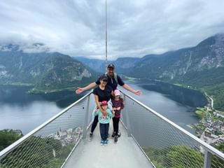 Famille de quatre personnes sur plateforme d'observation métallique surplombant le lac de Hallstatt et les montagnes du Salzkammergut autrichien.