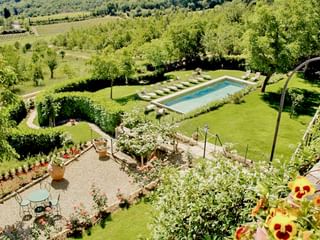 Vue aérienne du jardin de l'Hôtel Palazzo Squarcialupi avec piscine rectangulaire, transats, pelouses soignées, parterres de fleurs et paysage viticole.