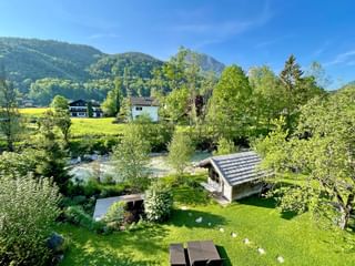 Vue sur jardin verdoyant de l'Hotel Bergrose avec pavillon en bois, pelouse et montagnes boisées en arrière-plan sous ciel bleu.