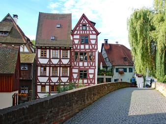 Rue pavée à Ulm avec maisons à colombages allemandes traditionnelles aux poutres rouge et blanc, pont de pierre et saule pleureur.
