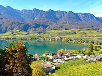 Vue panoramique du lac de Caldaro avec eau turquoise, vignobles, maisons de village et chaîne de montagnes sous ciel bleu près de Merano.