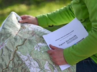 Randonneuse lisant une carte IGN et tenant un topoguide du circuit Vosges du Nord d'Espace Randonnée