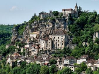Village médiéval construit sur une falaise rocheuse en Périgord Noir, avec des bâtiments en pierre descendant la colline et un château au sommet.