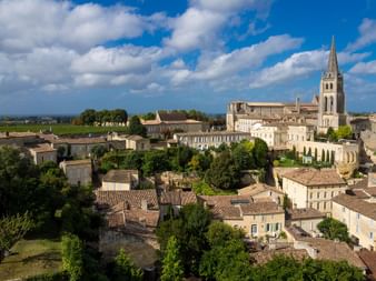 Vue aérienne de Saint-Émilion dans le vignoble bordelais montrant des bâtiments en pierre aux toits de tuiles, un clocher et des vignes.