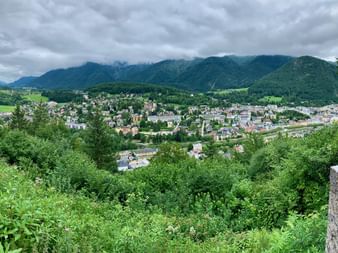 Vue surélevée de la ville de Bad Ischl nichée dans la vallée du Salzkammergut, entourée de montagnes boisées vertes sous un ciel nuageux.