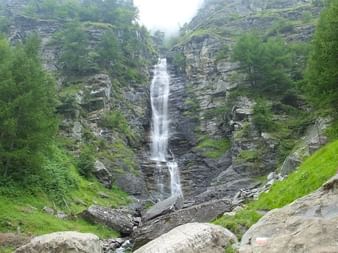 Grande cascade dévalant des falaises rocheuses stratifiées dans le Queyras, entourée d'une végétation verte luxuriante et d'arbres.