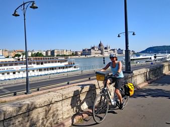 Cycliste avec casque sur la promenade fluviale à Budapest. Le Parlement hongrois visible de l'autre côté du Danube avec des bateaux de croisière.