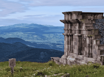 Structure en pierre ancienne au sommet herbeux du Puy de Dôme avec vue panoramique sur les montagnes volcaniques et vallées vertes d'Auvergne.