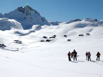 Groupe de raquetteurs traversant une vallée enneigée dans les montagnes du Queyras avec chalets traditionnels et pics sous ciel bleu.