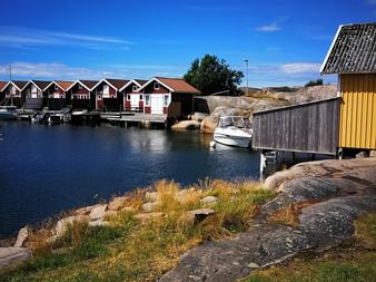 Cabanes de pêche rouges et blanches sur pilotis le long d'un port calme dans l'archipel de Stockholm. Rivage rocheux au premier plan.