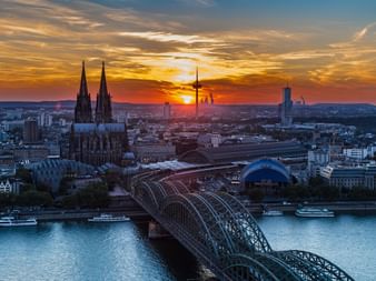 Vue aérienne de Cologne au coucher du soleil montrant la cathédrale gothique, le pont Hohenzollern sur le Rhin et l'horizon urbain.