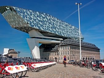 Maison du Port moderne à Anvers avec extension en verre en forme de diamant au-dessus d'une base historique en brique. Vélos partagés rouge et blanc au premier plan.