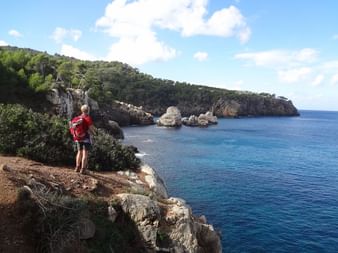 Randonneur sur sentier côtier de Majorque Randonneur avec sac à dos rouge sur falaise rocheuse de Majorque, contemplant les eaux turquoise de la Méditerranée et falaises calcaires.