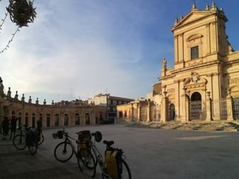 Cathédrale baroque avec façade ornée et clocher surplombant une place en pierre à Ispica, Sicile. Vélos garés au premier plan.
