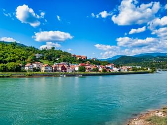 Ville de Visegrad le long du Danube avec maisons colorées, collines vertes et ruines de forteresse sur la colline sous ciel bleu et nuages blancs.