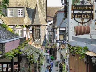 Rue pavée étroite à Rüdesheim avec maisons à colombages allemandes traditionnelles et enseignes de magasins ornées.