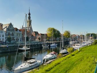Marina à Veere, Zélande avec voiliers amarrés le long du talus vert. Bâtiments historiques et clocher visibles de l'autre côté du port.
