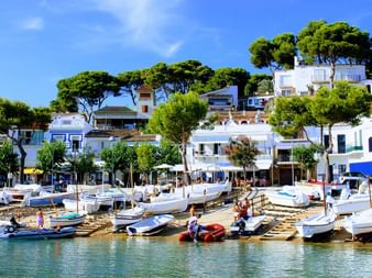 Bateaux blancs amarrés dans le port de Llafranc avec maisons méditerranéennes blanches sur la colline, pins verts et ciel bleu sur la Costa Brava, Espagne.