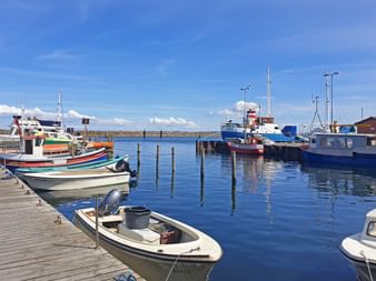 Port de Kerteminde avec bateaux de pêche colorés amarrés aux quais en bois. L'eau bleue reflète bateaux et mâts sous un ciel nuageux.