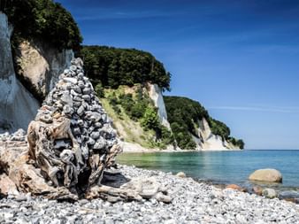 Falaises de craie blanche spectaculaires de Rügen s'élevant des eaux turquoise de la Baltique, avec plage rocheuse et cairn au premier plan.