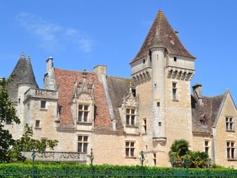 Château de Milandes, château Renaissance avec tours coniques et murs en pierre, entouré de haies vertes sous un ciel bleu en Périgord Noir.