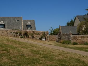 Maisons en pierre avec toits d'ardoise et lucarnes sur l'île de Bréhat dans les Côtes-d'Armor, Bretagne. Pelouse et murs de pierre bordent un chemin sous ciel bleu.