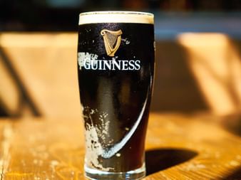 Un verre pinte plein de Guinness stout avec sa bière noire distinctive et sa mousse blanche crémeuse épaisse, avec le logo harpe iconique sur le verre.
