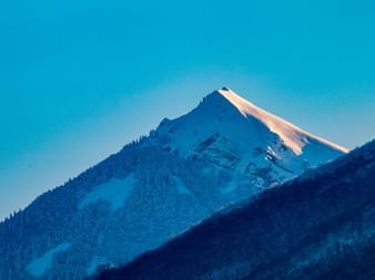 Sommet enneigé de la Pointe du Galoppaz dans le massif des Bauges avec lueur alpine rosée contre le ciel bleu crépusculaire.