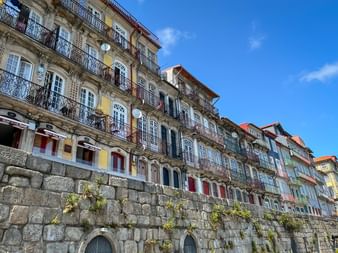 Bâtiments historiques colorés avec balcons ornés s'élevant au-dessus d'un vieux mur de pierre à Porto. Les façades sont jaunes, blanches et bleues.