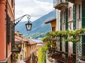 Bâtiments colorés avec balcons à Bellagio surplombant le lac de Côme. Montagnes en arrière-plan sous un ciel nuageux.