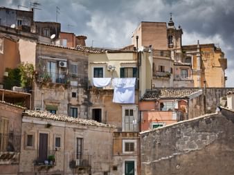 Bâtiments historiques colorés à Raguse avec façades patinées, balcons et linge suspendu. Un clocher d'église est visible parmi les structures.