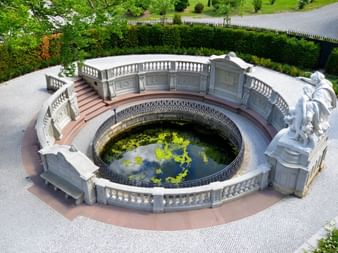 Monument de la source du Danube à Donaueschingen Monument circulaire en pierre marquant la source du Danube à Donaueschingen avec balustrades ornées, statues et bassin central à l'eau verte.