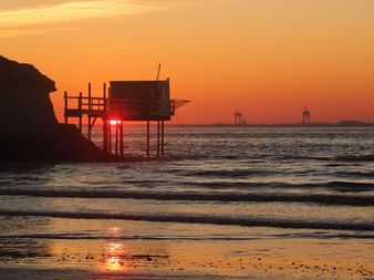 Coucher de soleil sur l'estuaire de la Gironde avec cabane de pêche traditionnelle sur pilotis en silhouette. L'eau calme reflète la lumière dorée.