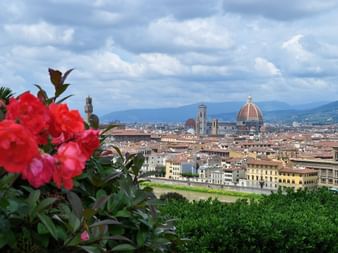 Fleurs rouges au premier plan avec le panorama de Florence derrière, montrant le dôme en terre cuite du Duomo et les clochers sous un ciel nuageux.