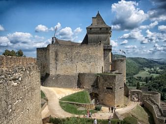 Château médiéval de Castelnau avec murs en pierre et tour dominant la vallée verte du Périgord Noir. Visiteurs dans la cour.