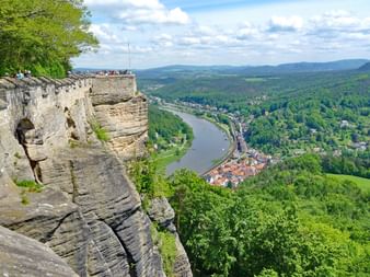 Vue des falaises de grès Suisse saxonne Formations rocheuses spectaculaires en grès de Suisse saxonne surplombant la vallée de l'Elbe avec collines boisées et petite ville sous ciel nuageux.