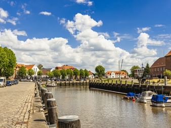 Port de St. Michaelisdonn avec canal, bollards en bois le long du quai pavé, bateaux amarrés et bâtiments traditionnels sous ciel bleu.