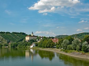 Château de Gundelsheim et rivière Neckar Vue pittoresque de Gundelsheim avec château historique sur la colline surplombant le Neckar, entouré de vignobles et forêts vertes.