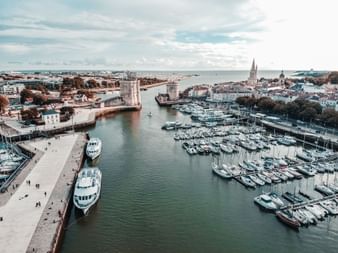 Vue aérienne du Vieux-Port de La Rochelle avec marina, tours historiques à l'entrée du port, bateaux amarrés aux quais et panorama urbain.