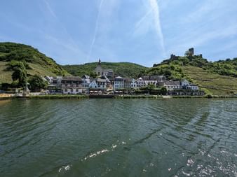 Bernkastel-Kues le long de la Moselle avec maisons à colombages traditionnelles, collines couvertes de vignobles et ruine de château médiéval.