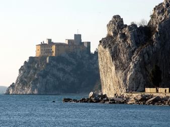 Le Château de Duino perché au sommet de falaises calcaires blanches surplombant l'Adriatique, avec une côte rocheuse et des eaux bleues calmes.