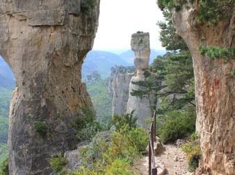 Sentier de randonnée étroit avec garde-corps métallique entre hautes formations calcaires aux Gorges du Tarn et Jonte, vallée boisée en contrebas.