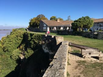 Mur de fortification en pierre avec canon historique surplombant l'estuaire de la Gironde dans le Médoc. Maisons traditionnelles et pelouses vertes derrière les murs.