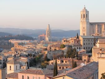 Vue panoramique de la vieille ville de Gérone avec clocher et cathédrale au coucher du soleil. Bâtiments historiques aux toits de terre cuite et montagnes.