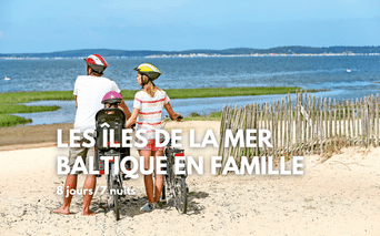 Famille avec vélos sur plage sablonneuse de la mer Baltique. Deux adultes et enfant avec casques près d'une clôture en bois, eau bleue visible.