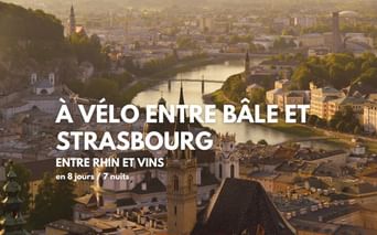 Vue aérienne de Bâle avec le Rhin, des ponts et des clochers à l'heure dorée. Texte: circuit à vélo entre Bâle et Strasbourg.