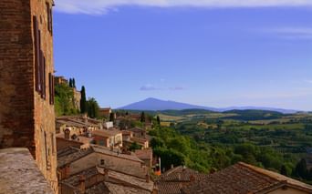 Vue de Montepulciano montrant des toits en terre cuite, des cyprès et des collines toscanes avec une montagne lointaine sous un ciel bleu.